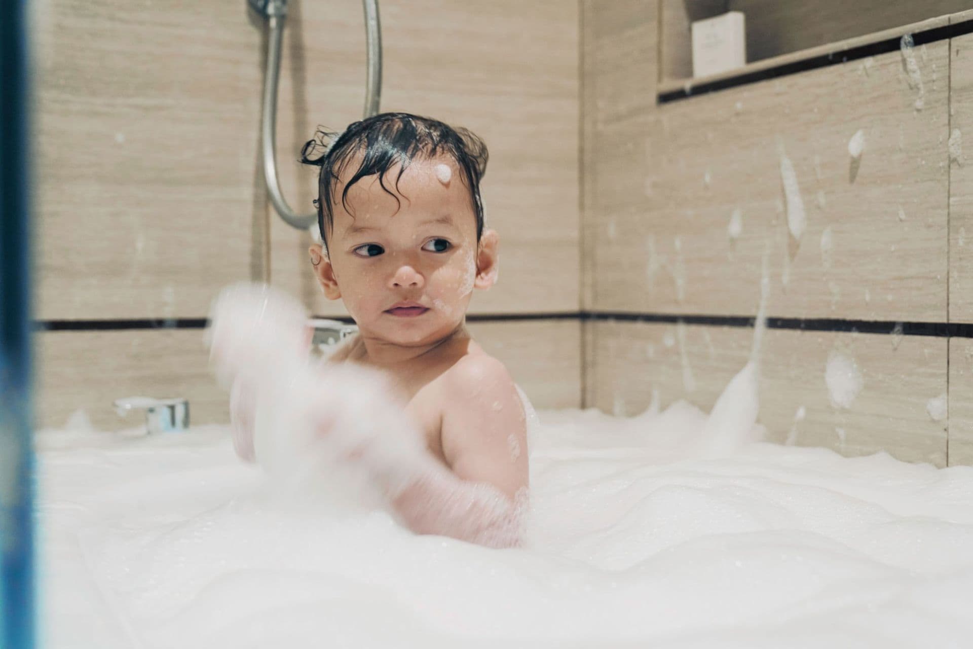 Kid plays with bubbles in a bathtub with acrylic paneled walls