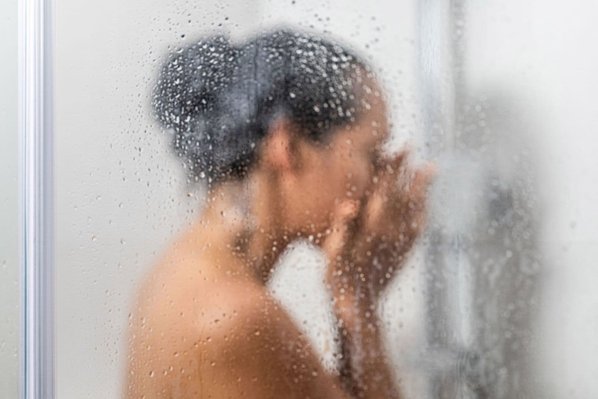 woman showering behind wet glass shower door